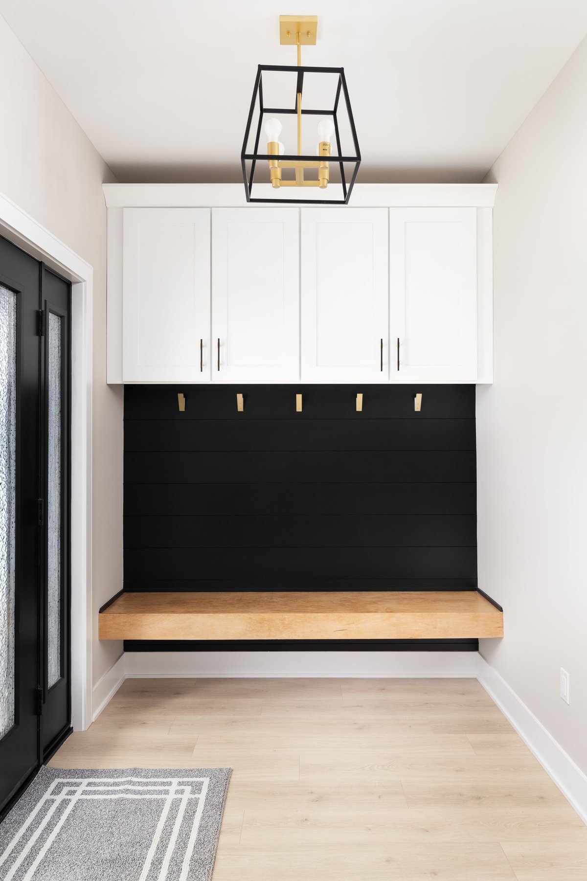 A modern farmhouse entryway with bench seating, black shiplap, white cabinets, gold coat hooks