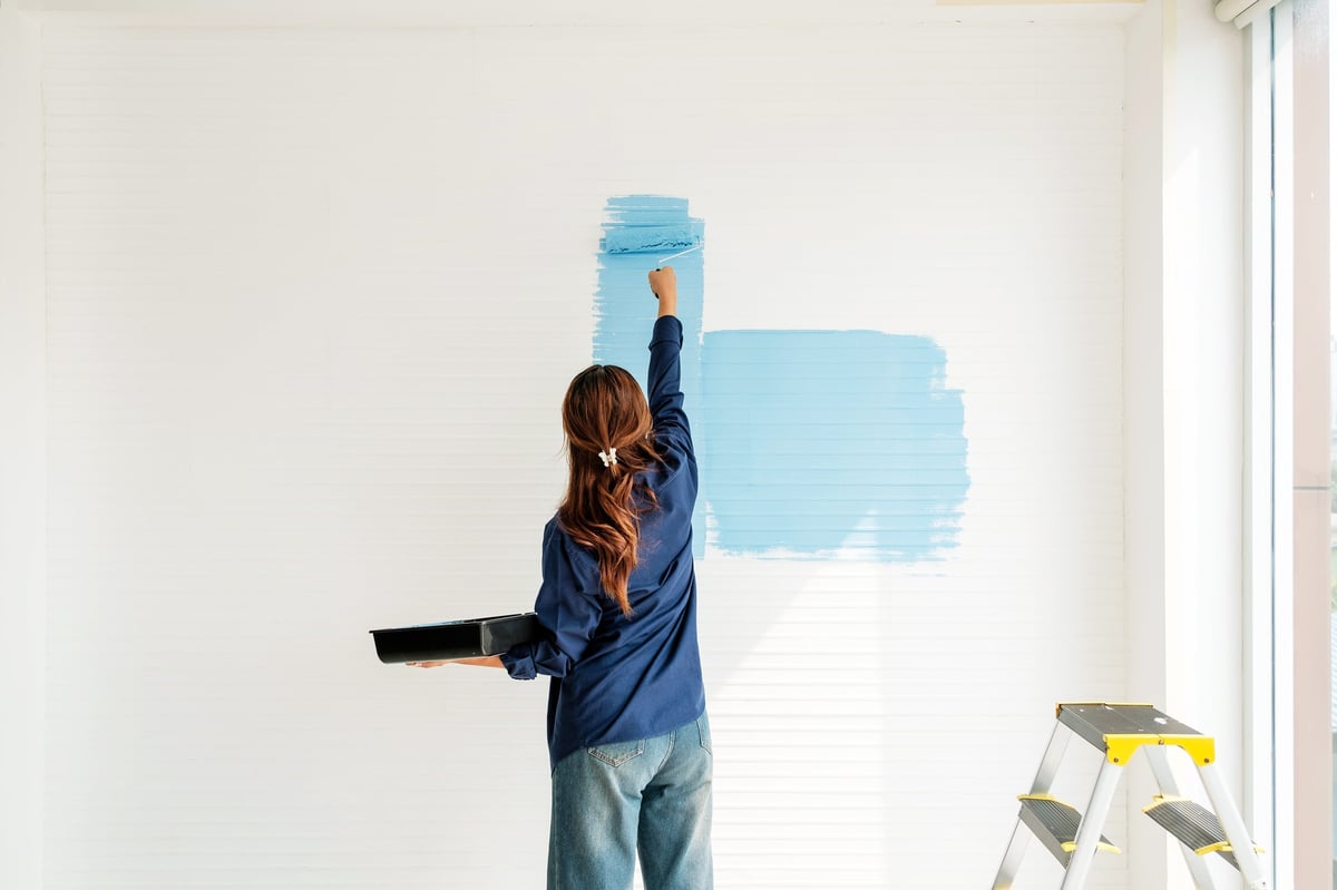 Woman painting white wall with blue paint using roller