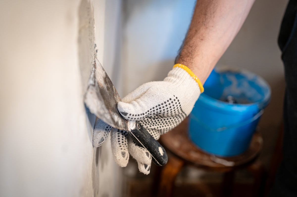 Worker using putty knife to press patching compound into wall hole