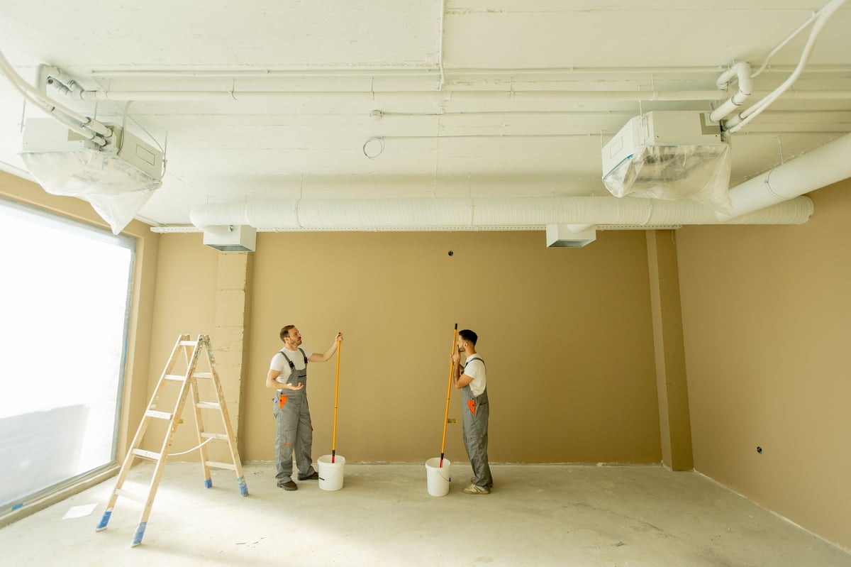 Two painters working on beige wall in bright room