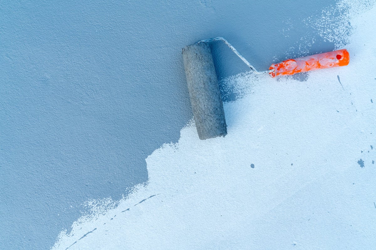 Paint roller applying blue paint on textured concrete surface