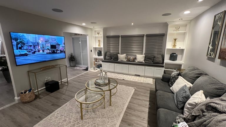 Modern living room with mounted TV, gray sofa, round glass coffee tables, and kitchen area visible in background