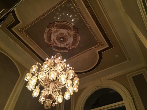 Ornate crystal chandelier hanging from decorative ceiling medallion in classical interior with coffered ceiling details