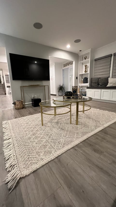 Modern living room with mounted TV above fireplace, round glass coffee table on patterned rug, and built-in white cabinetry